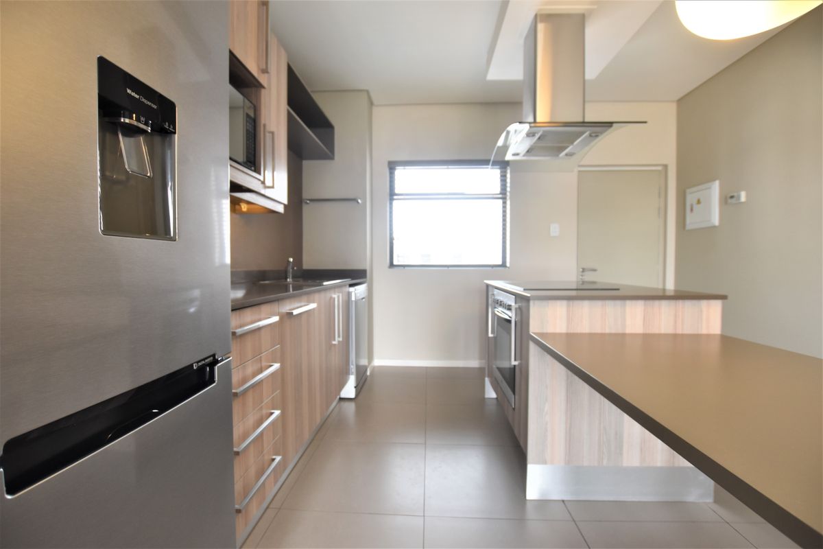 Modern kitchen featuring wood-finish cabinetry, stone countertops, stainless steel appliances, and a functional island layout with integrated hob and oven.