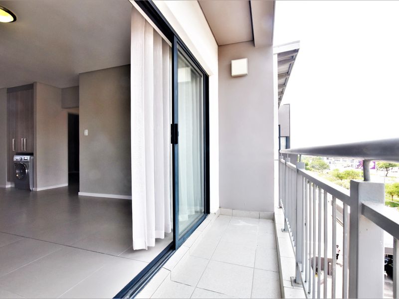 A modern apartment balcony featuring tiled flooring, a metal balustrade, and seamless access to the interior living area with built-in cabinetry.