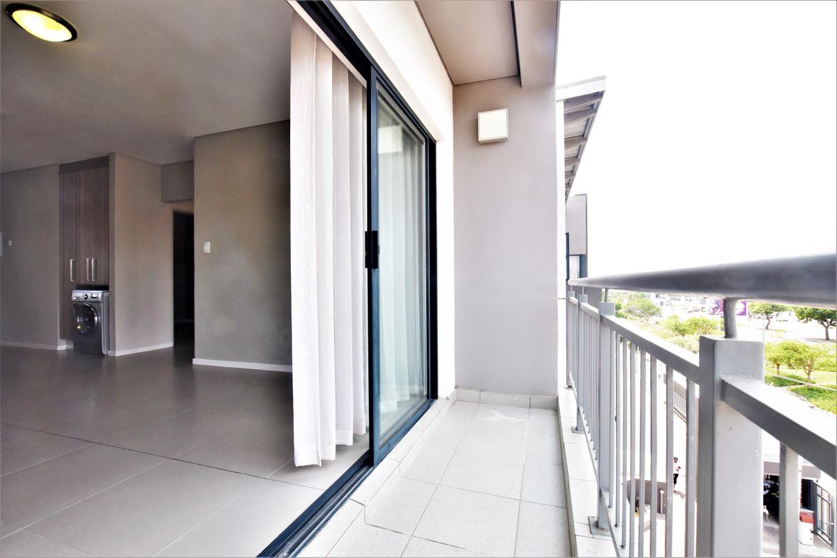 A modern apartment balcony featuring tiled flooring, a metal balustrade, and seamless access to the interior living area with built-in cabinetry.