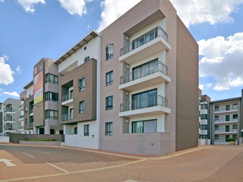A modern multi-story apartment complex featuring contemporary facade design, private balconies with metal railings, and a paved driveway entrance.