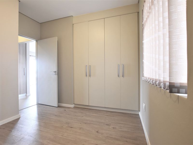 A bright, empty bedroom featuring neutral walls, laminate flooring, and a large built-in wardrobe with modern handles.