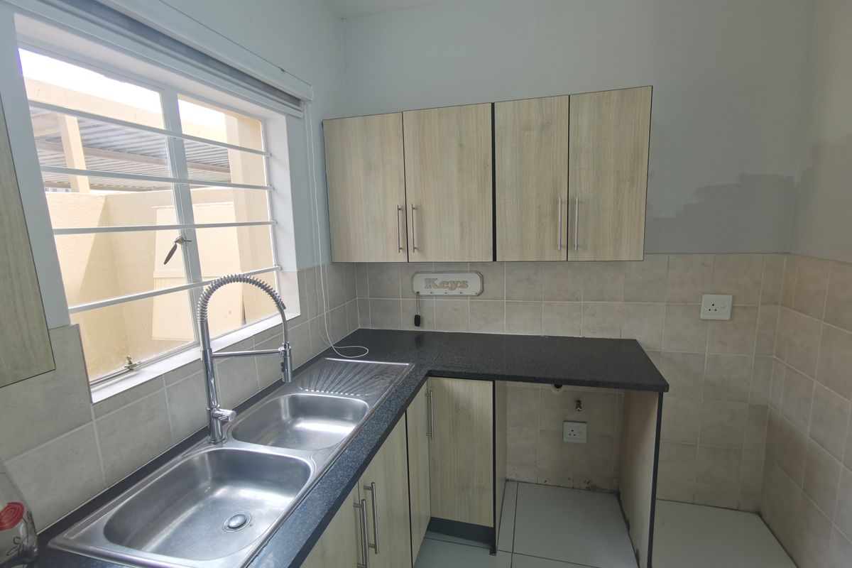 A functional kitchen area featuring light wood-finish cabinetry, granite countertops, a double stainless steel sink, and tiled splashbacks with space for an under-counter appliance.
