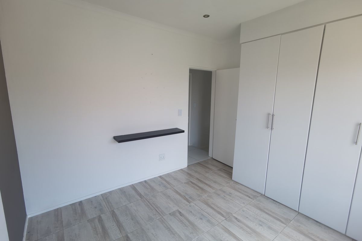A clean, empty bedroom featuring modern light-toned tiled flooring, built-in white cupboards, and recessed ceiling lighting.