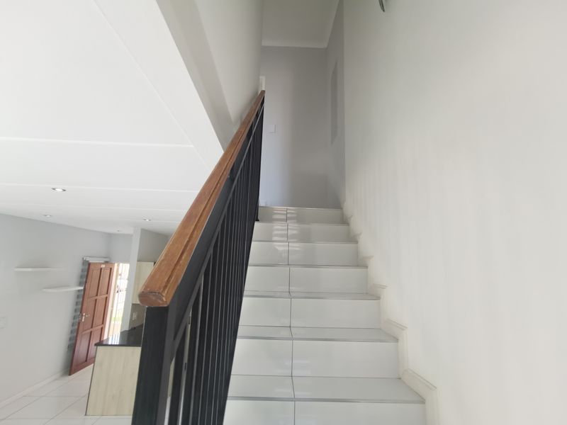 A clean, modern staircase featuring white tiled steps, a black metal balustrade with a wooden handrail, leading to an upper level.
