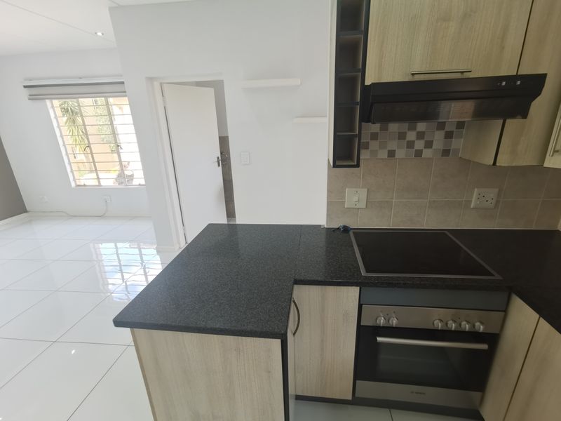 Modern open-plan kitchen featuring granite countertops, built-in oven, hob, and extractor fan, flowing into a bright, tiled living area.