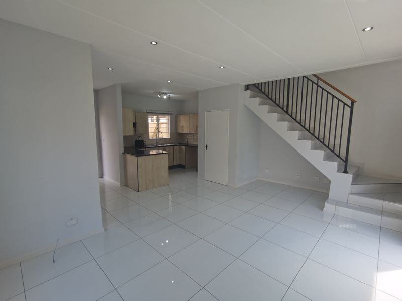 Spacious open-plan living area featuring glossy tiled floors, recessed lighting, and a modern staircase, seamlessly flowing into a functional kitchen with granite countertops.