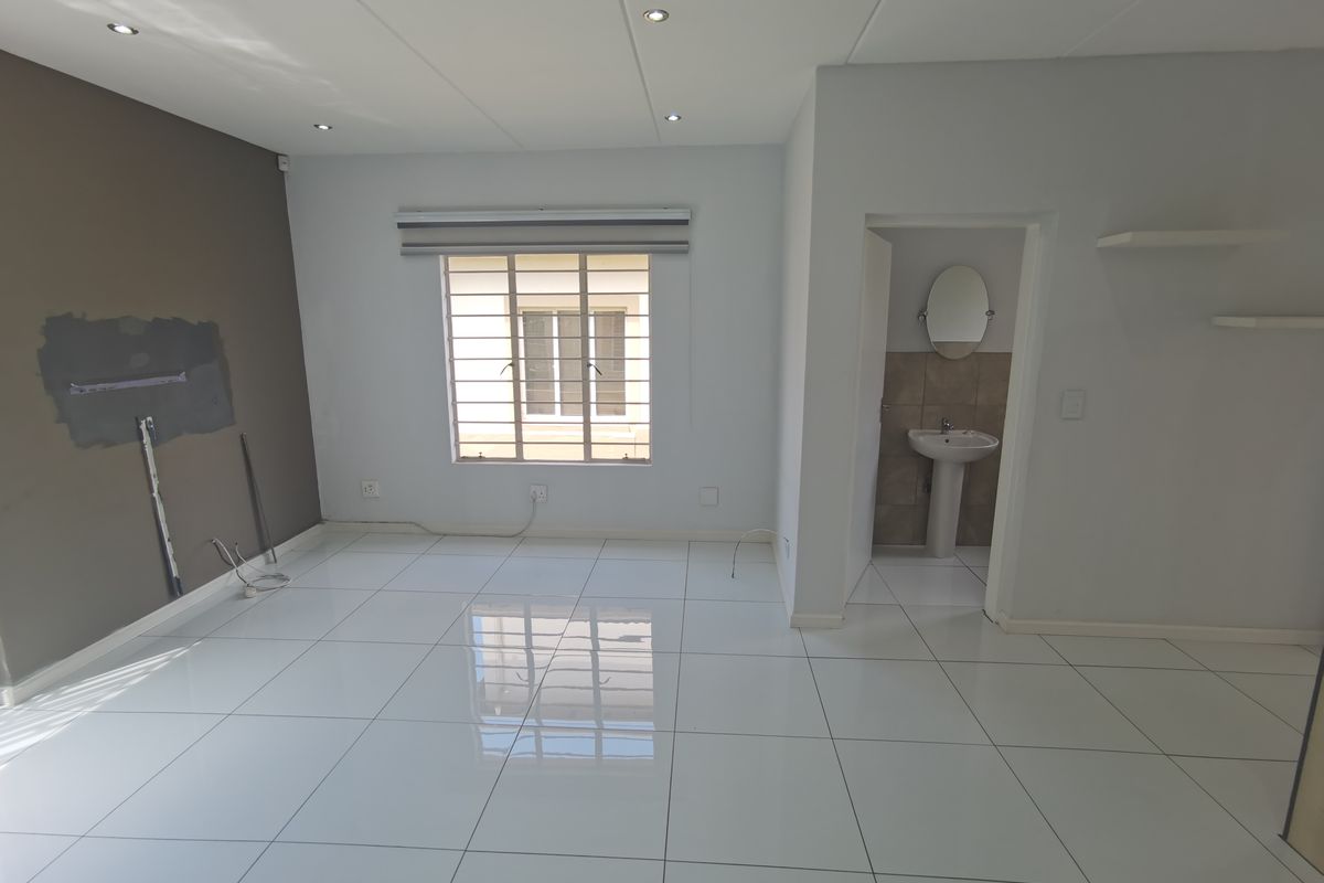 An open-plan living area featuring polished white floor tiles, recessed lighting, and an adjoining small bathroom with a pedestal basin.