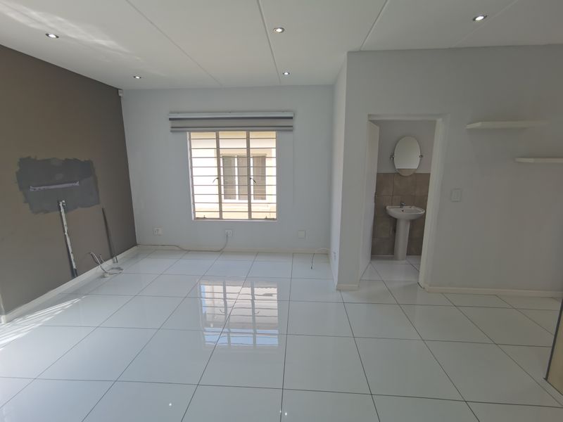 An open-plan living area featuring polished white floor tiles, recessed lighting, and an adjoining small bathroom with a pedestal basin.
