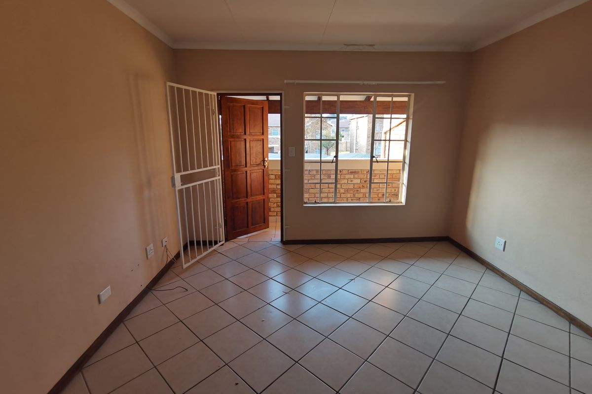 An empty living room featuring tiled flooring, a security gate at the entrance, and a window providing natural light.