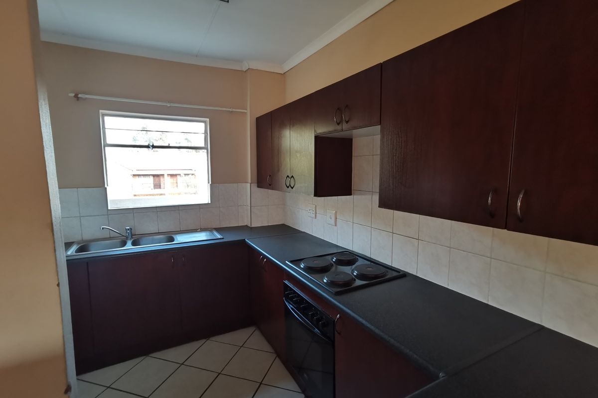 A functional kitchen featuring dark wood-finish cabinetry, a built-in electric hob and oven, double sink, and tiled flooring.