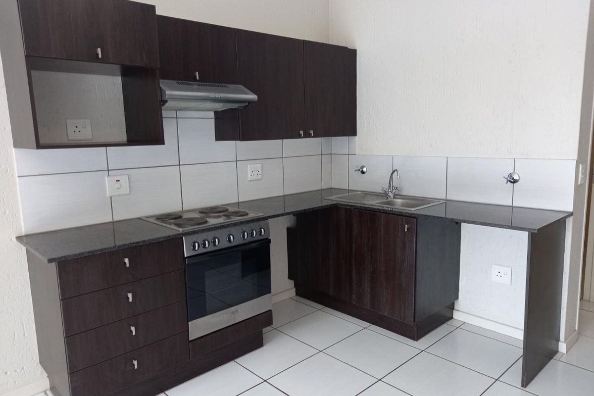 A clean, functional kitchen featuring dark wood cabinetry, granite countertops, a built-in electric stove with extractor fan, and a stainless steel double sink.