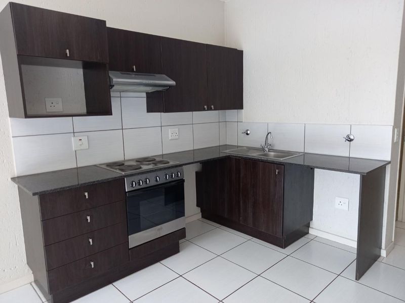 A clean, functional kitchen featuring dark wood cabinetry, granite countertops, a built-in electric stove with extractor fan, and a stainless steel double sink.