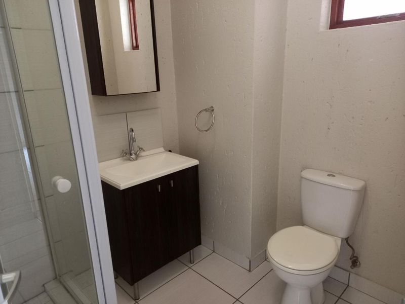 A functional bathroom featuring a vanity cabinet with basin, a toilet, and a glass-enclosed shower with tiled flooring.