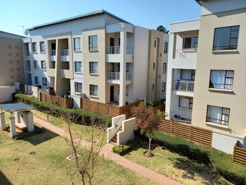 An elevated view of a modern apartment complex featuring landscaped gardens, paved walkways, and private balconies with timber fencing.