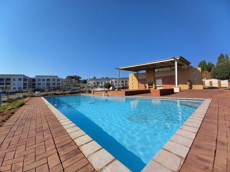 A well-maintained communal swimming pool area featuring a paved deck and a covered outdoor entertainment structure.