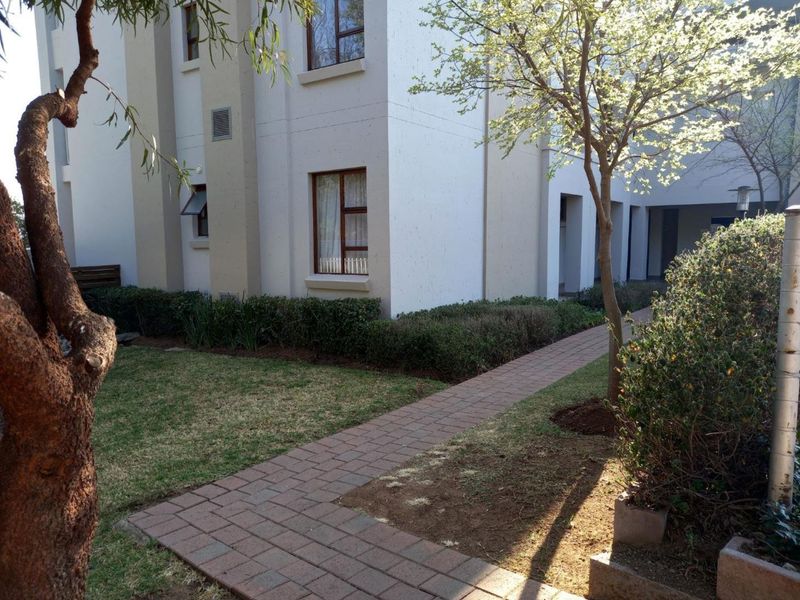 Exterior view of the apartment building featuring a paved walkway, landscaped garden areas, and multi-story facade with aluminum window frames.