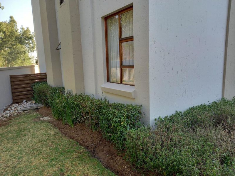 A view of the rear exterior wall featuring a timber window frame, adjacent garden bed, and timber slat fencing.