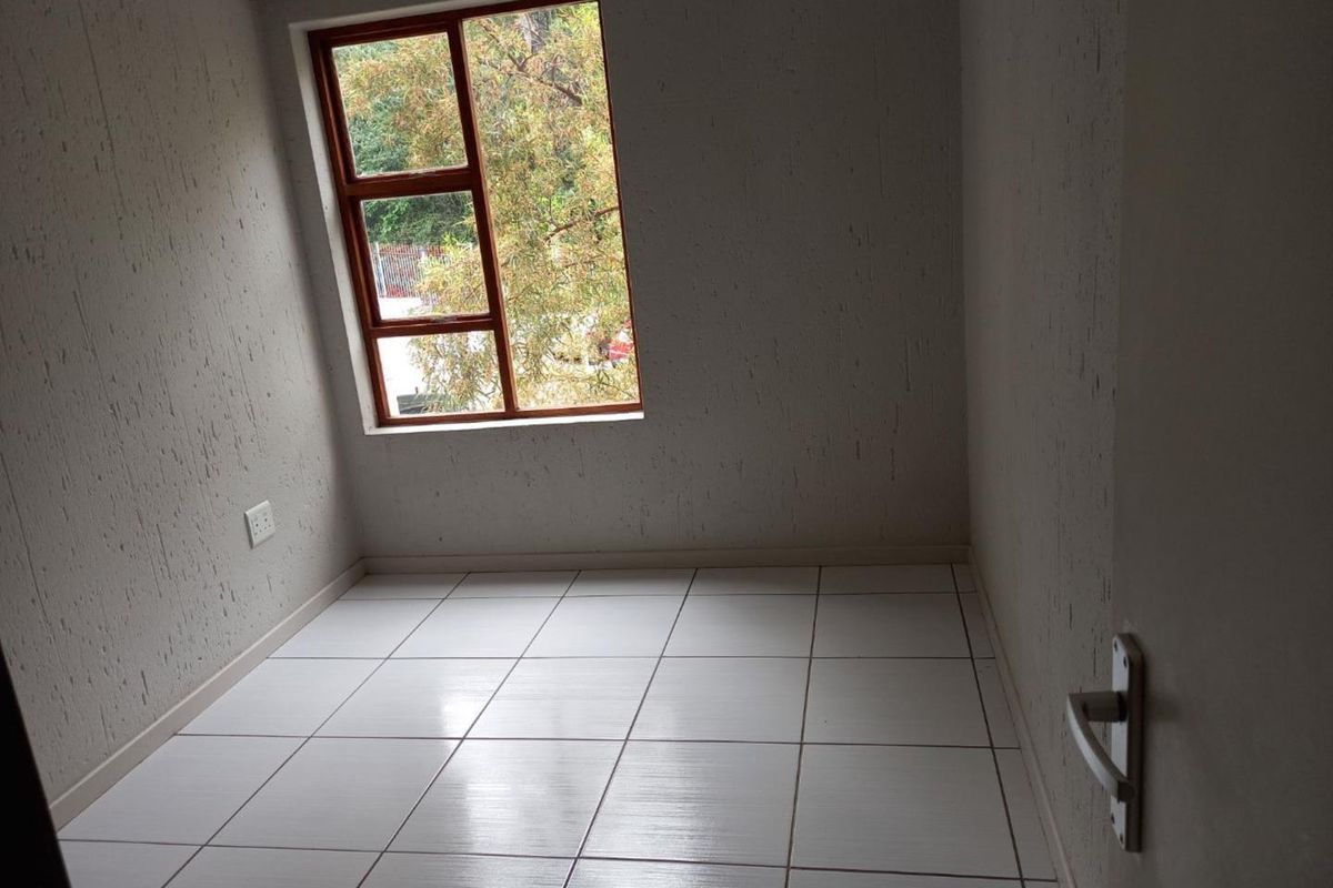 A vacant bedroom featuring white tiled flooring, textured walls, and a window with a wooden frame, offering a clean and neutral space.