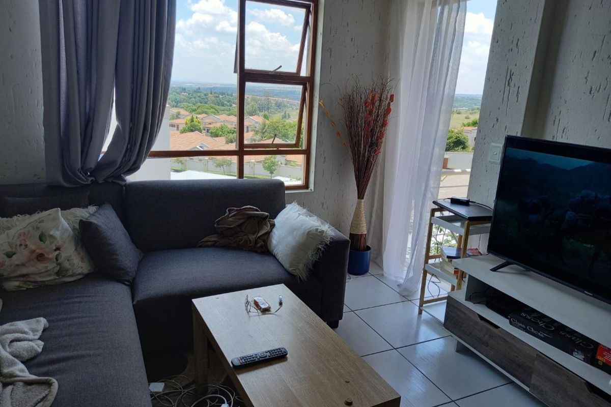 A bright living room featuring tiled flooring, textured walls, and large windows providing natural light and scenic views with access to an outdoor area.