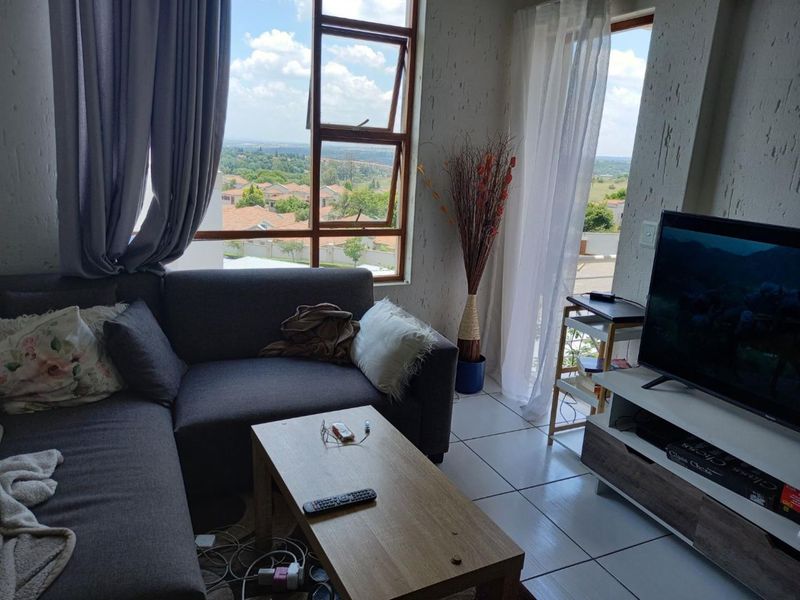 A bright living room featuring tiled flooring, textured walls, and large windows providing natural light and scenic views with access to an outdoor area.