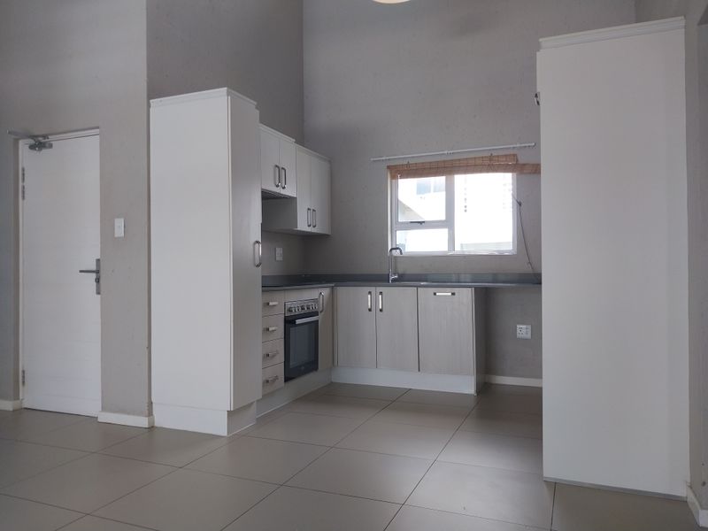 A clean, modern kitchen featuring built-in cabinetry, an integrated oven and hob, and neutral tiled flooring in an open-plan layout.