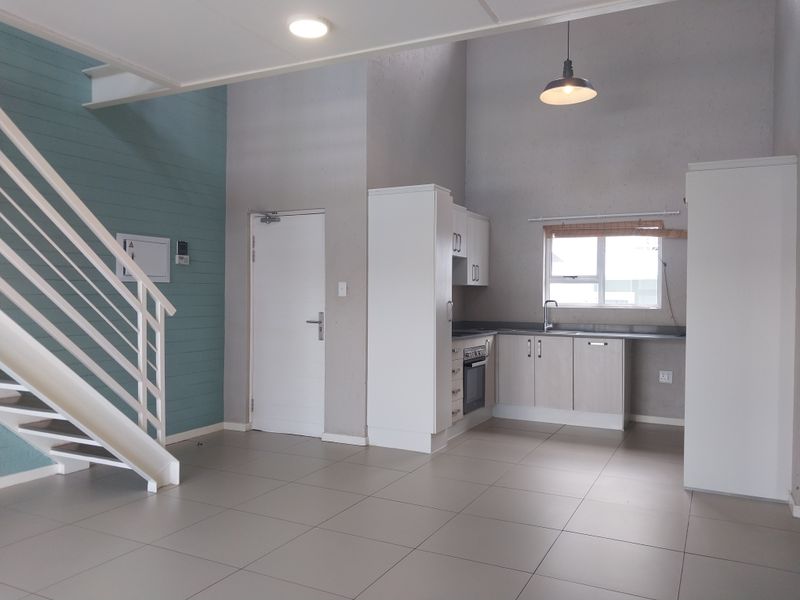 Open-plan living area featuring a modern kitchen with built-in appliances, tiled flooring, and a staircase leading to the upper level.