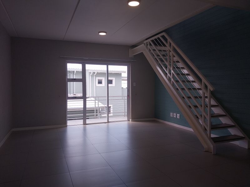 An open-plan living area featuring modern tiled flooring, a staircase leading to an upper level, and a sliding glass door opening to a balcony.