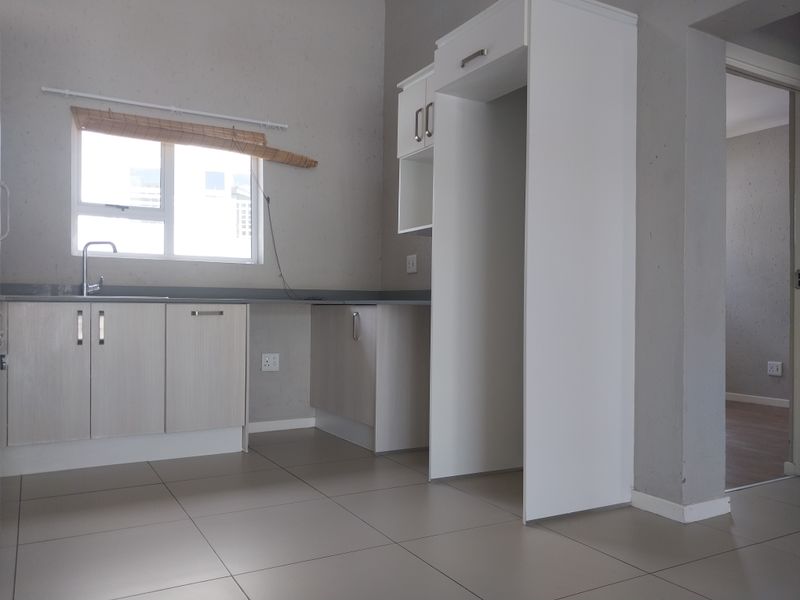 A clean, modern kitchen featuring light-toned built-in cabinetry, a stainless steel sink, tiled flooring, and a dedicated space for a refrigerator.