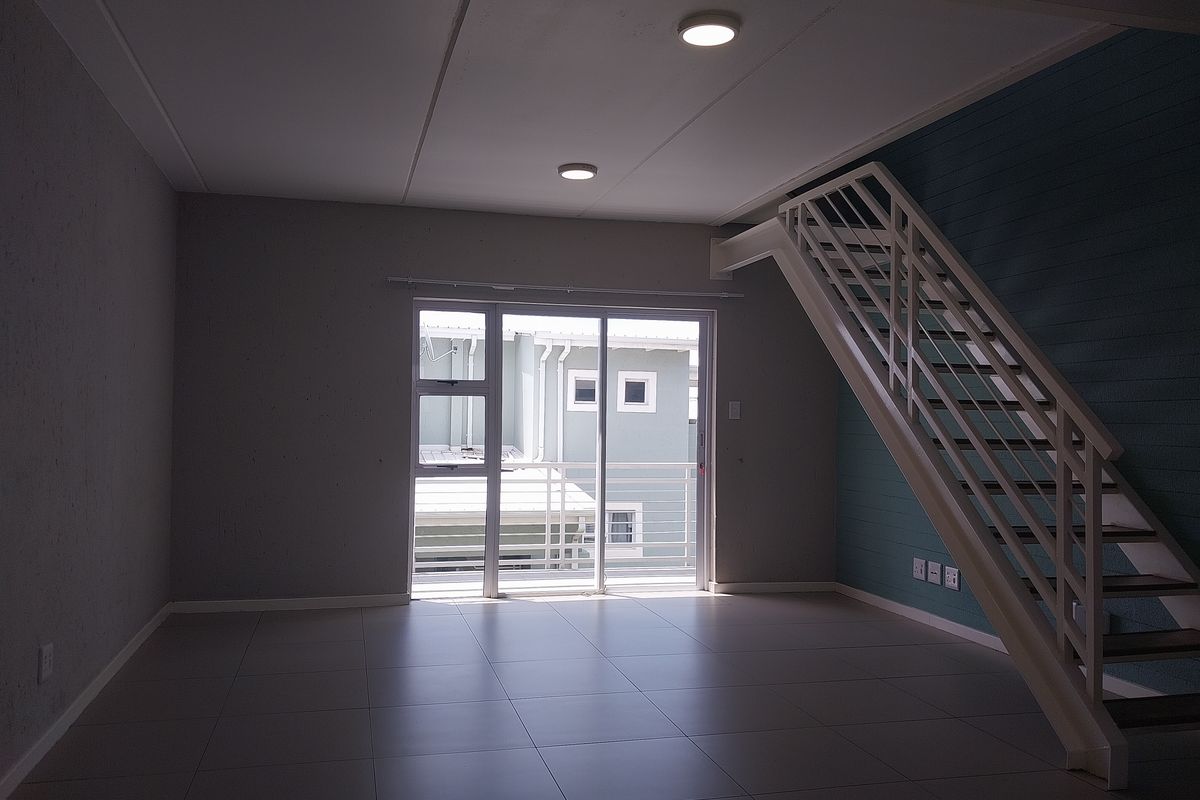 An open-plan living area featuring tiled flooring, a staircase, and a sliding glass door leading to an outdoor space.