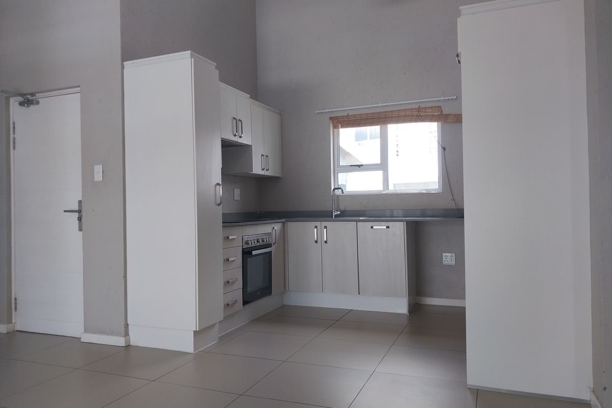 A clean, functional kitchen featuring built-in cabinetry, an integrated oven and hob, and tiled flooring in an open-plan apartment setting.