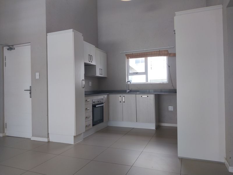 A clean, functional kitchen featuring built-in cabinetry, an integrated oven and hob, and tiled flooring in an open-plan apartment setting.