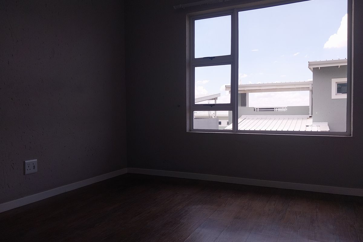 An empty bedroom featuring laminate flooring, neutral walls, and a large aluminium-framed window providing natural light.
