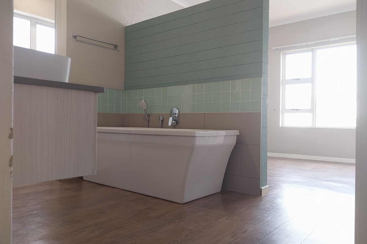 Modern open-plan bathroom featuring a sleek freestanding bathtub, wall-mounted basin, and contemporary tiled partition wall with wood-look flooring.