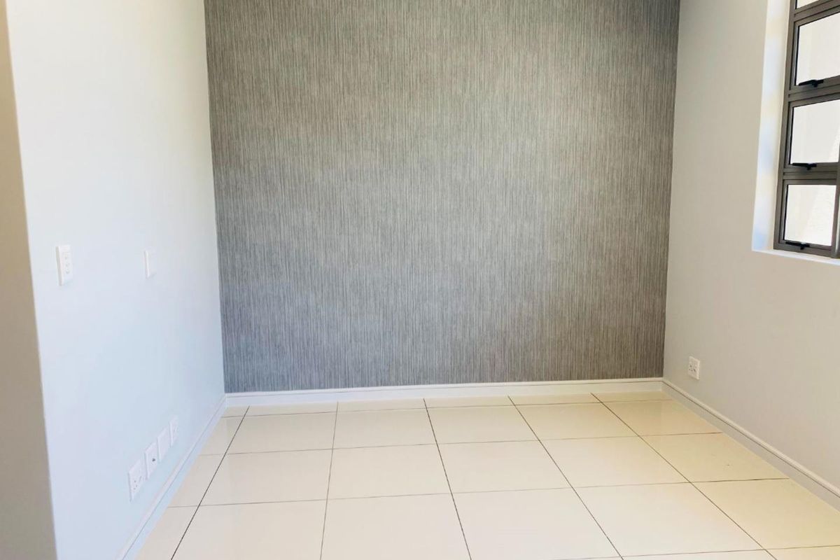 A bright, empty bedroom featuring neutral tiled flooring and a modern grey textured feature wall with an aluminium window.