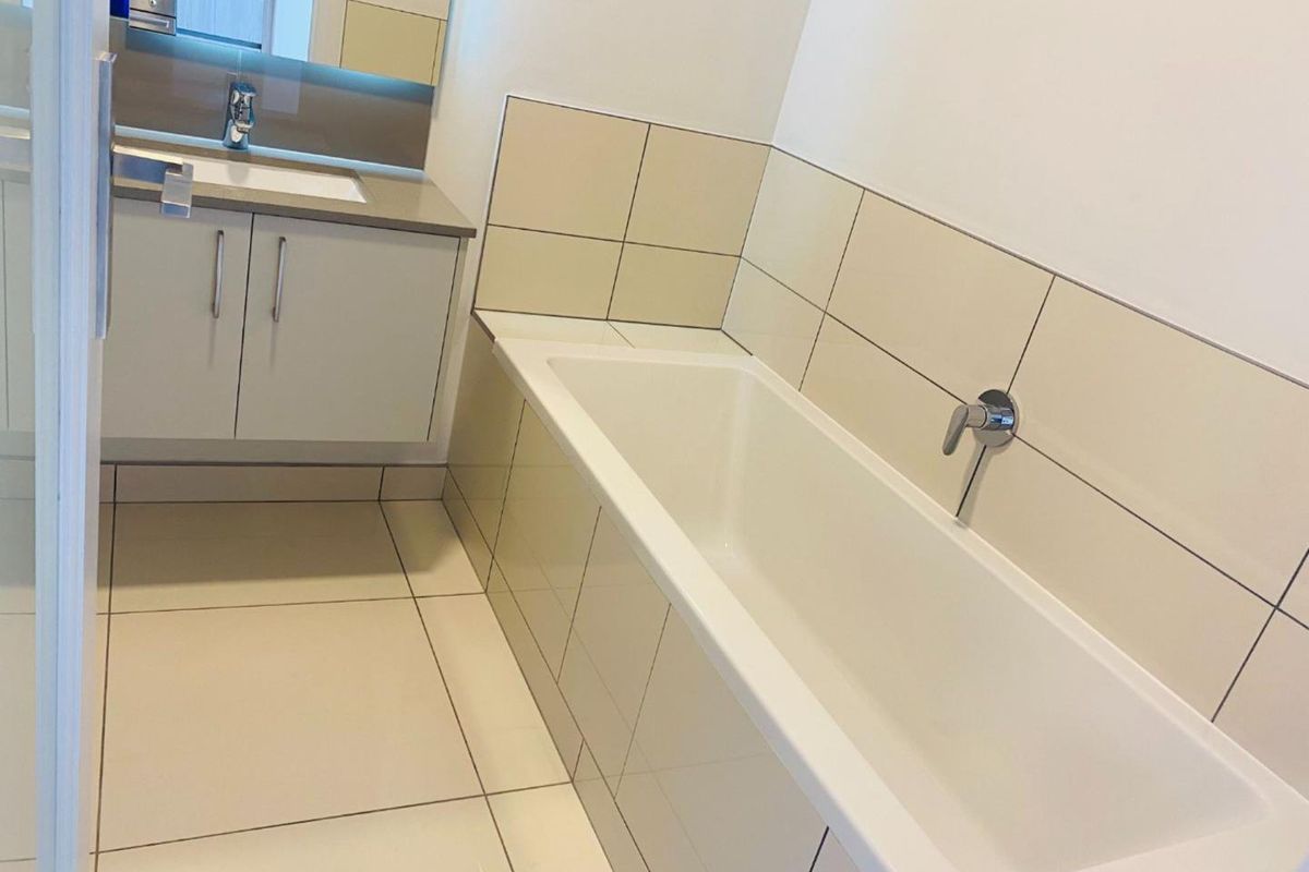 A clean, modern bathroom featuring a built-in bathtub, tiled surround, and a vanity unit with an integrated sink and mirror.