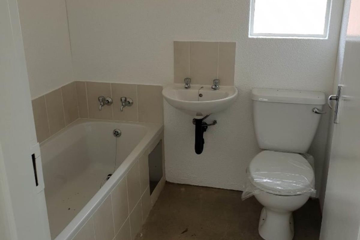 A compact bathroom featuring a built-in bathtub, wall-mounted basin, and toilet, currently requiring final flooring and minor finishing touches.