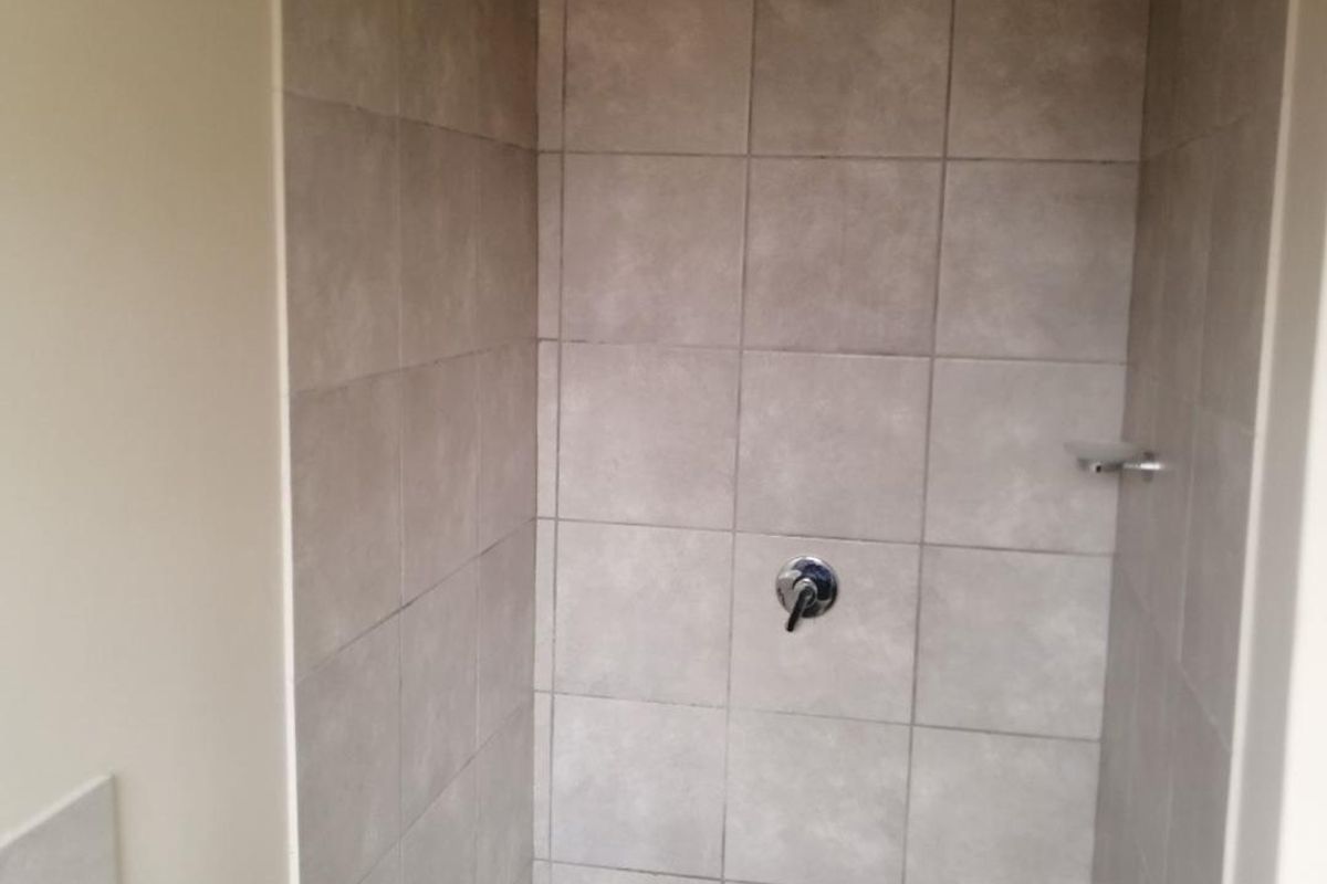 A functional shower enclosure featuring neutral wall tiling, a built-in soap dish, and a standard chrome shower mixer and head.