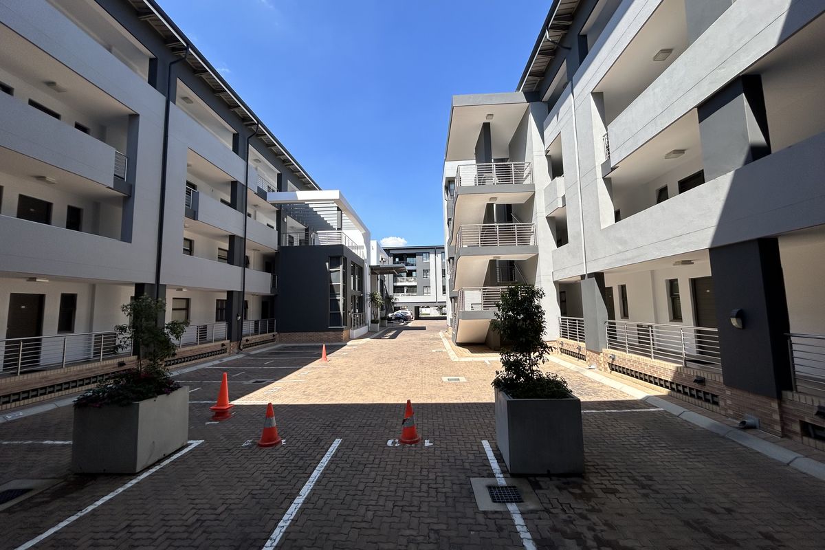 Exterior view of a modern apartment complex courtyard featuring paved parking bays, metal staircases, and balconies with steel railings.