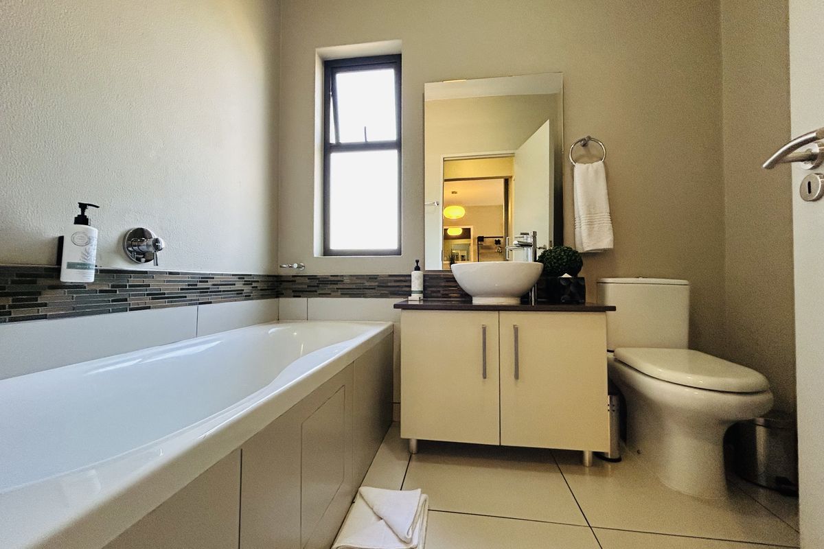 A well-maintained bathroom featuring a built-in bathtub, a modern vanity with a vessel sink, a toilet, and tiled flooring with a decorative mosaic backsplash.
