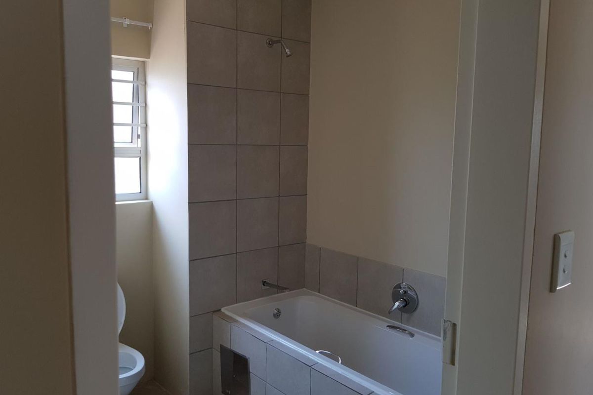 A functional bathroom featuring a built-in bathtub with shower mixer, tiled splashback, and a standard toilet.