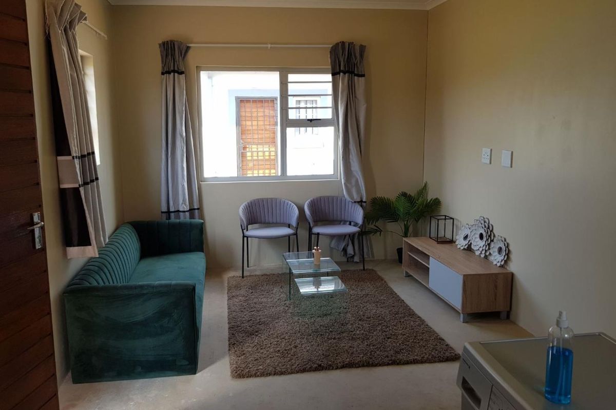 A compact living room featuring neutral walls, a large window with curtains, and tiled flooring, providing a functional and comfortable space.