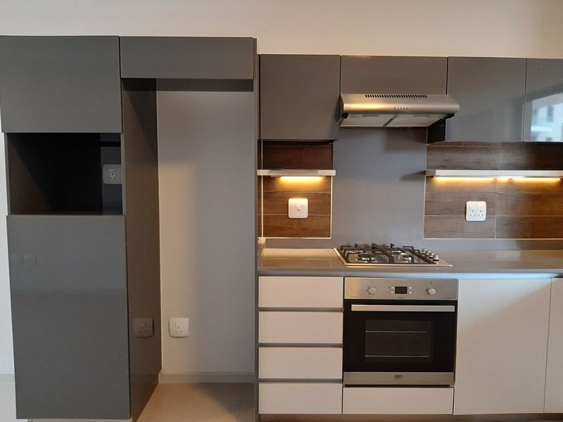 Modern kitchen featuring sleek grey and white cabinetry, stone countertops, a built-in gas hob, electric oven, and integrated extractor fan with under-cabinet lighting.