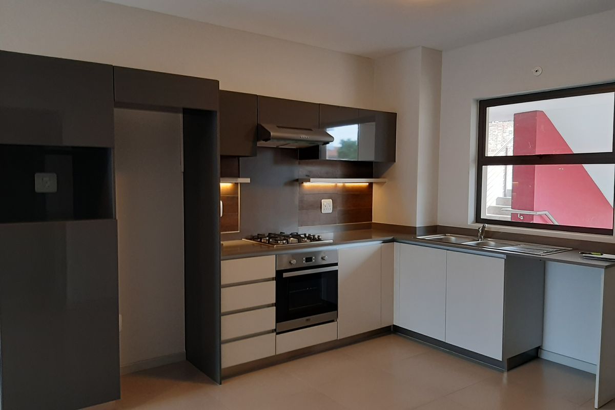 Modern kitchen featuring sleek two-tone cabinetry, built-in gas hob, electric oven, extractor fan, and a stainless steel double sink with ample counter space.