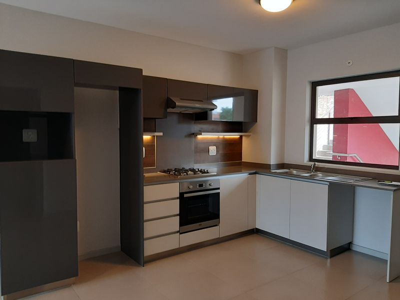 Modern kitchen featuring sleek two-tone cabinetry, built-in gas hob, electric oven, extractor fan, and a stainless steel double sink with ample counter space.