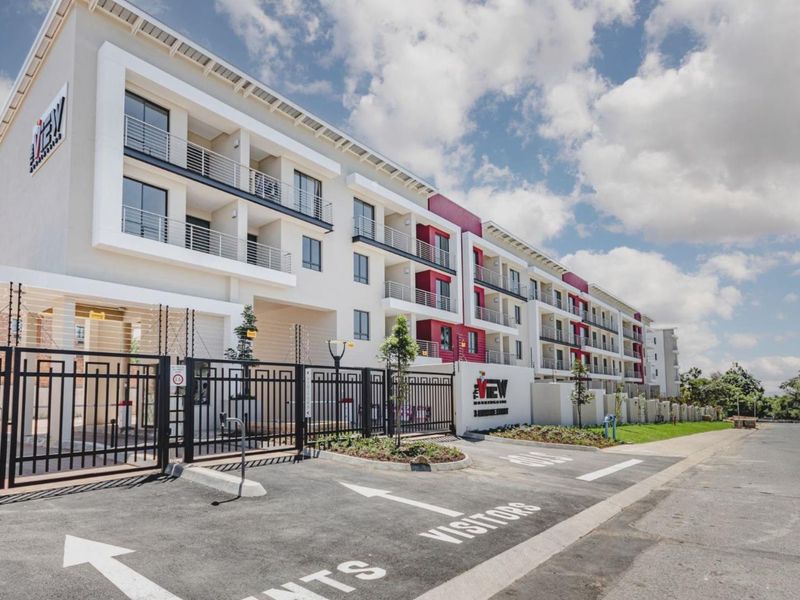Modern apartment complex exterior featuring a secure gated entrance, paved visitor parking, and multi-level balconies with contemporary architectural design.