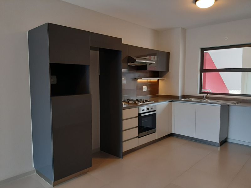 Modern kitchen featuring sleek two-tone cabinetry, built-in gas hob, electric oven, extractor fan, and stainless steel sink with tiled flooring.