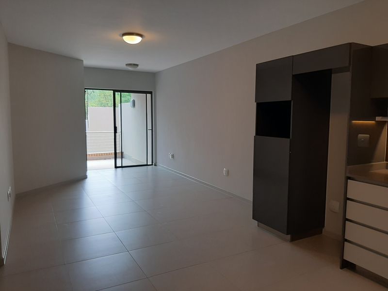 An open-plan living and kitchen area featuring neutral tiled flooring, modern built-in cabinetry, and a sliding glass door leading to an outdoor space.