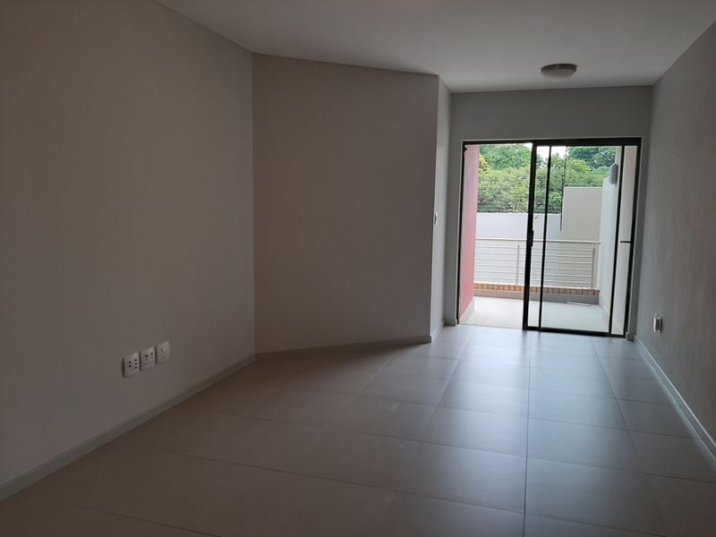 An empty, well-maintained living area featuring neutral tiled flooring and a sliding glass door providing access to an outdoor balcony.