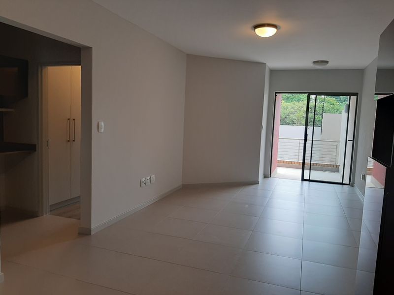 An open-plan living area featuring neutral tiled flooring, clean walls, and a sliding glass door leading to a private balcony.