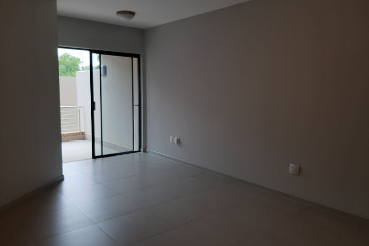 An empty, neutral-toned living area featuring large format floor tiles and a sliding glass door providing access to an outdoor balcony space.